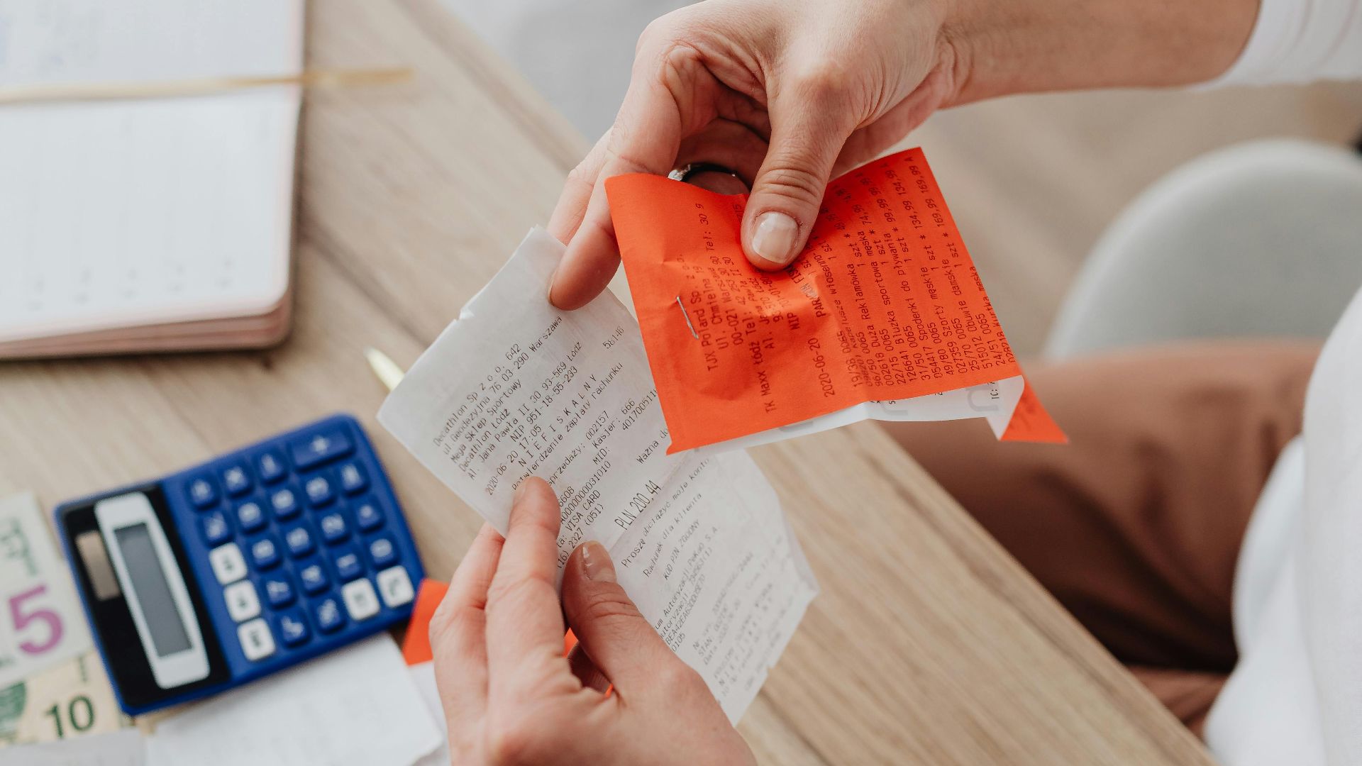 Top view of person organizing finances with calculator, receipts, and notes at desk.