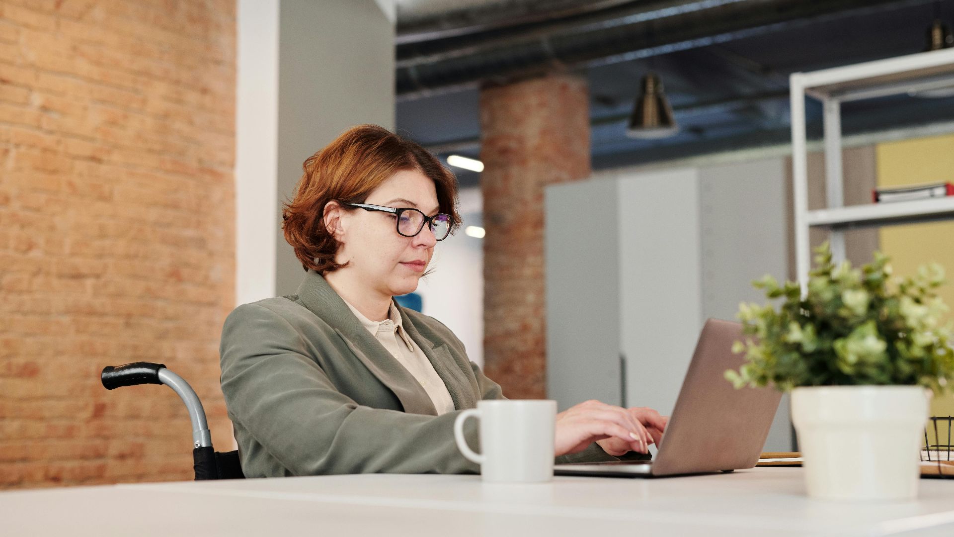 Professional woman in a wheelchair working on a laptop at a contemporary workspace.
