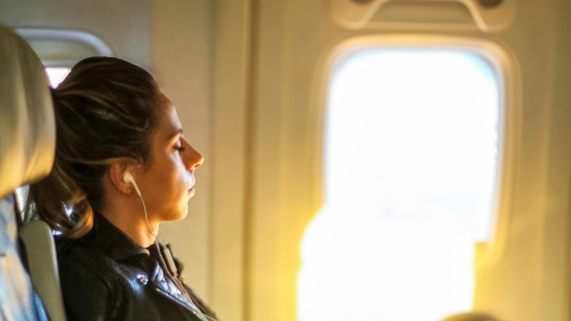 A woman enjoys a tranquil moment on a flight, gazing out the window with headphones on.