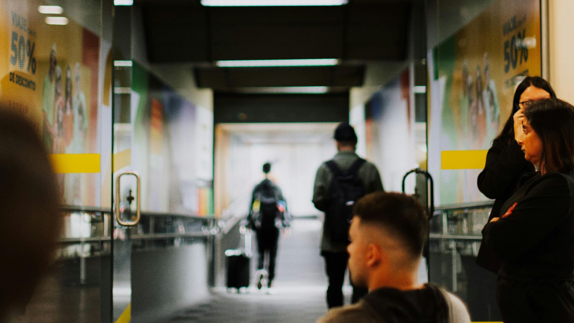 Travelers waiting at a bustling airport gate with a focus on the entrance and sign.