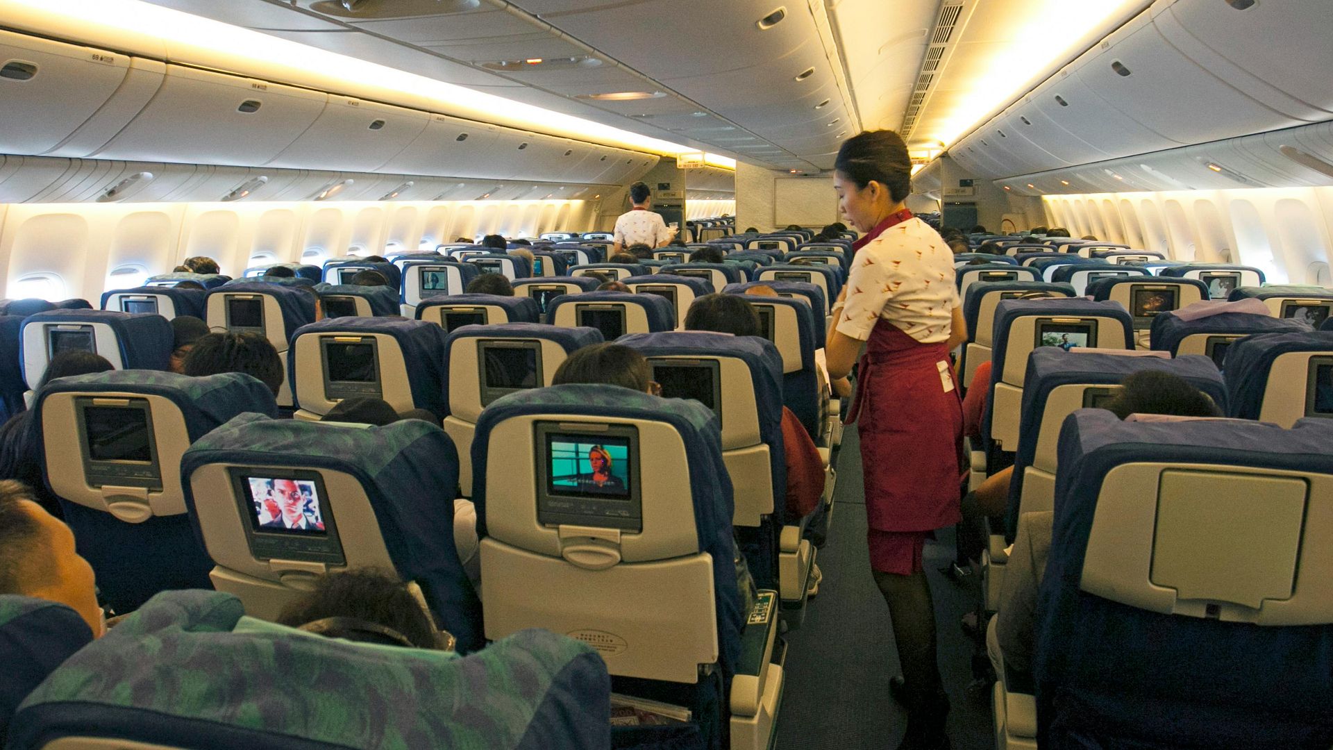 Flight attendant assisting passengers in a busy airplane cabin, ensuring a comfortable travel experience.