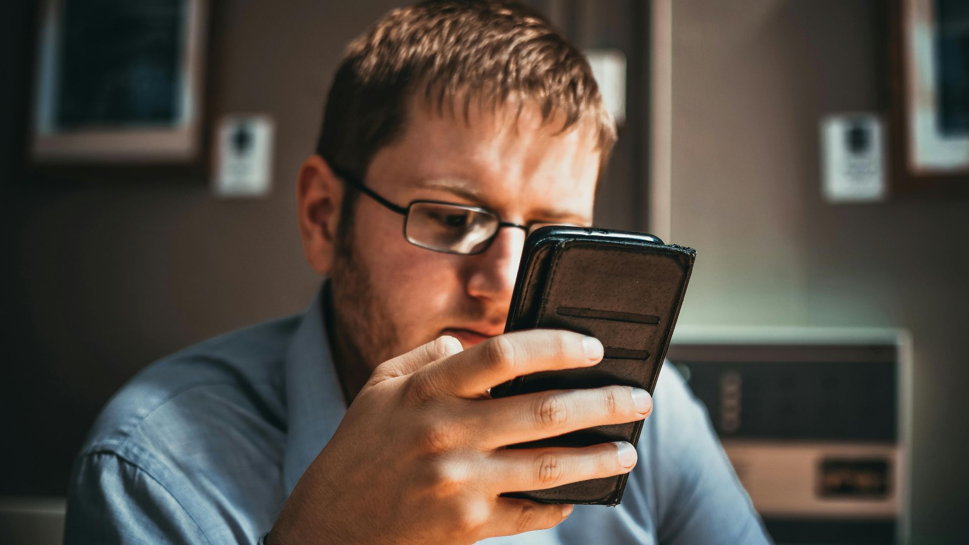 Serious businessman wearing glasses focused on smartphone in a modern office setting.