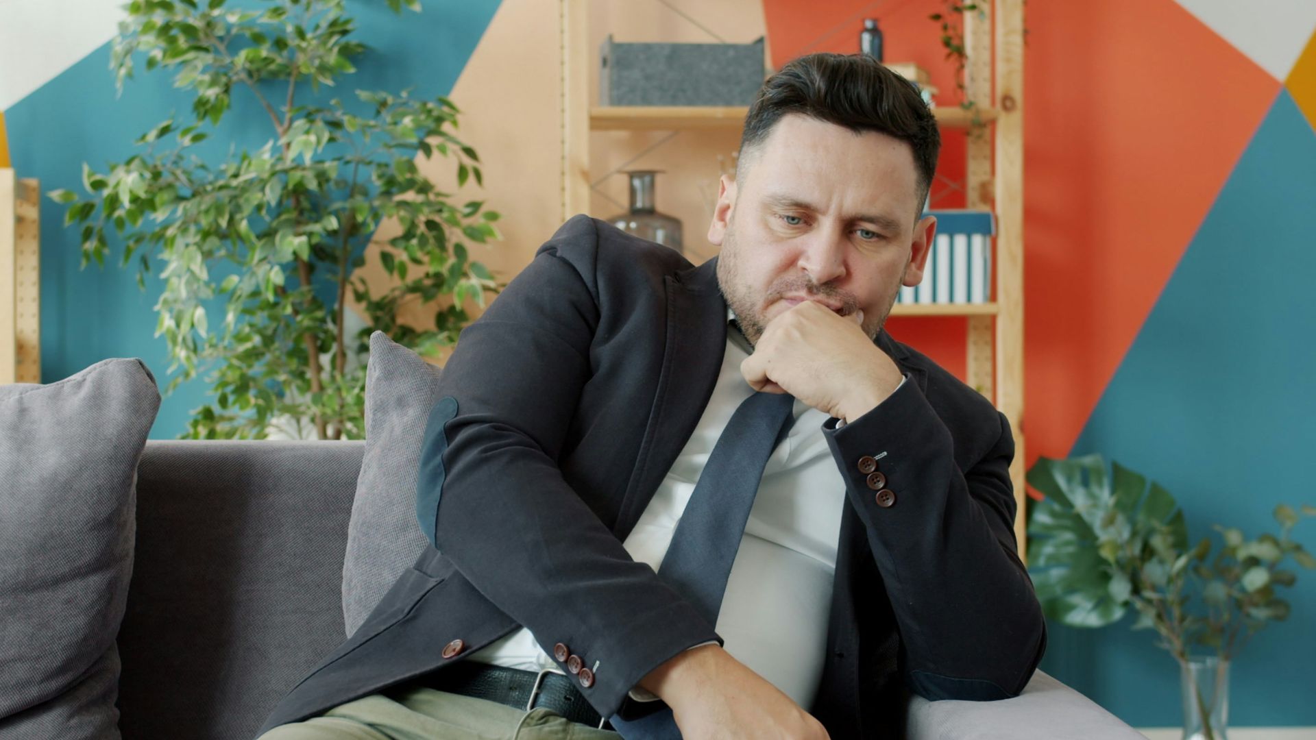 Man in suit sitting on couch looking thoughtful.