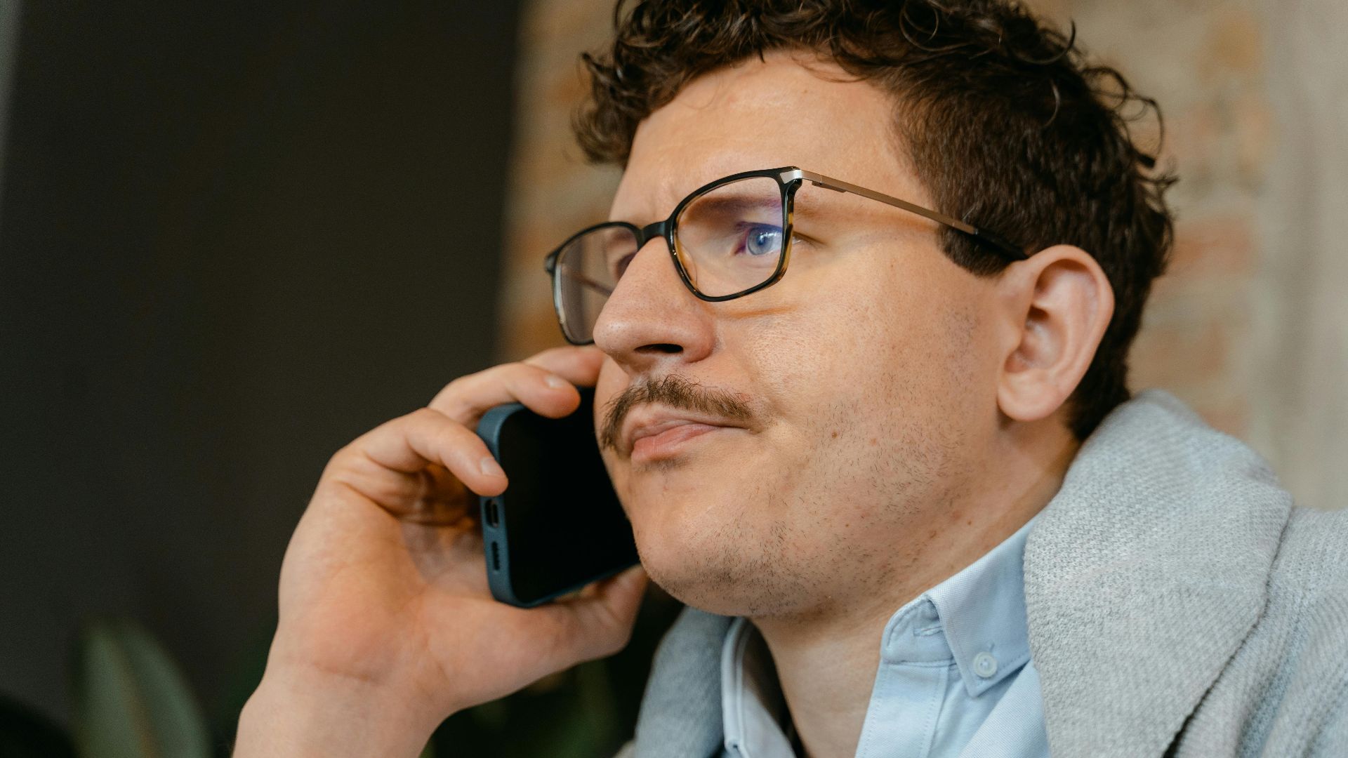 Man with glasses and mustache making a smartphone call indoors.