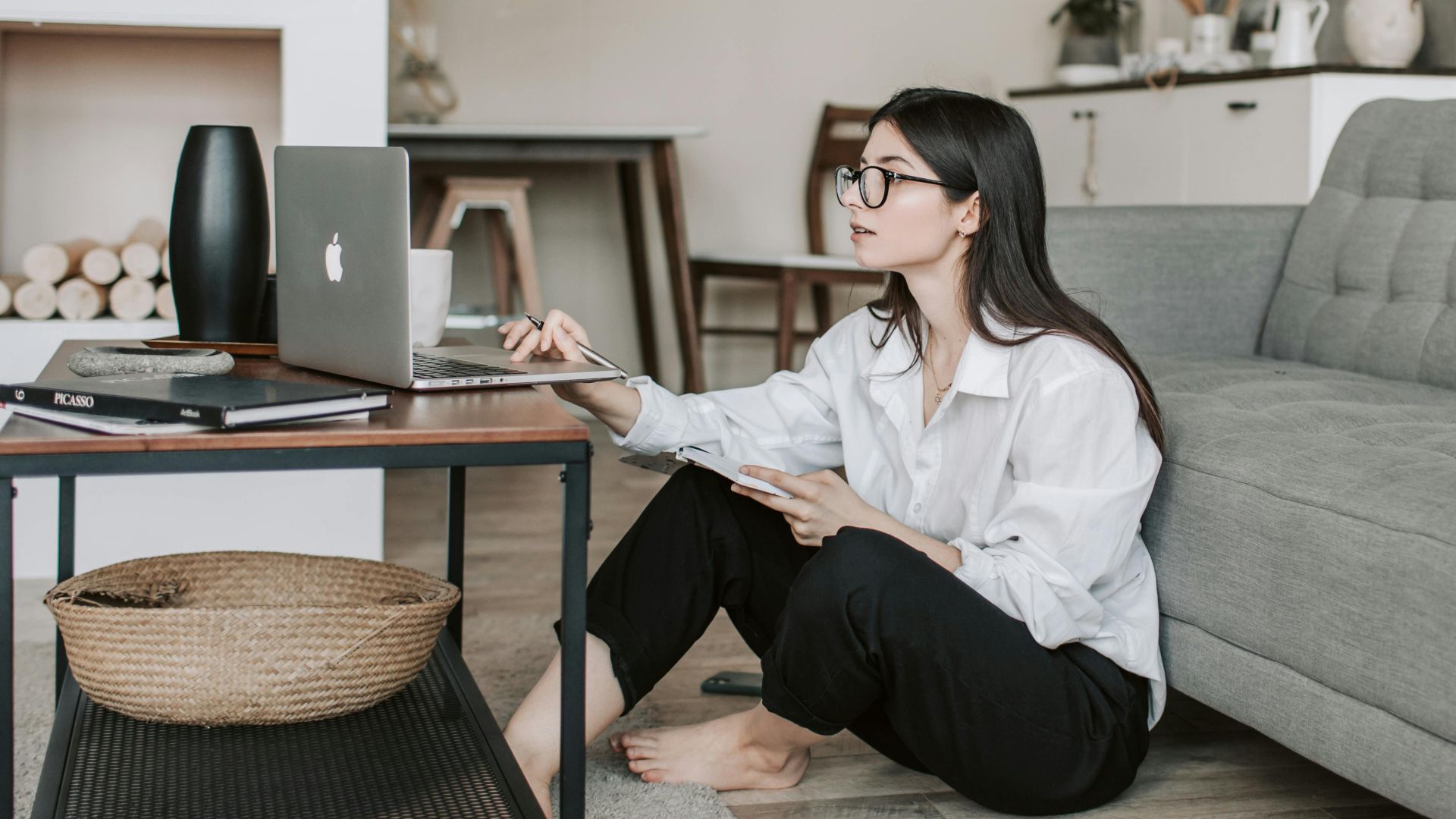 Asian woman working on laptop from cozy living room, showcasing modern home office setup.