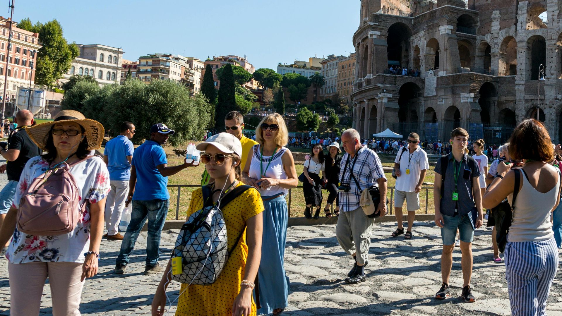 Tourists wander around the iconic Colosseum in Rome on a clear summer day, capturing memories.