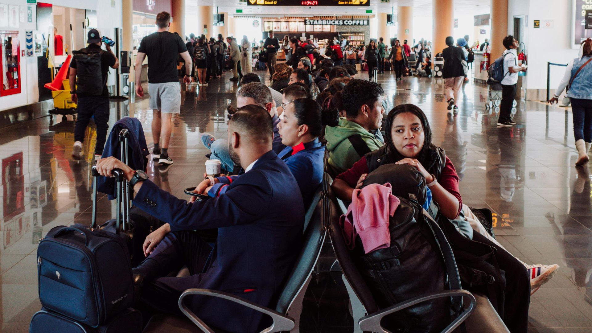 Passengers waiting in a busy airport terminal seating area, with luggage in the modern airport.