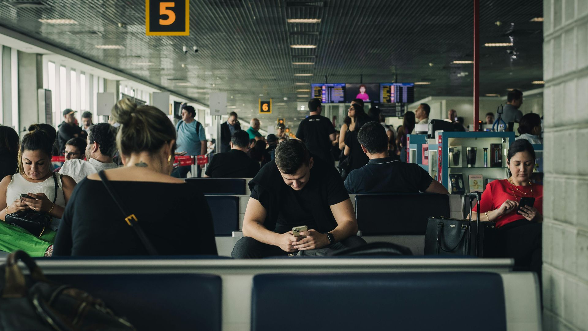 Travelers seated and waiting at São Paulo airport terminal, engaging with smartphones.