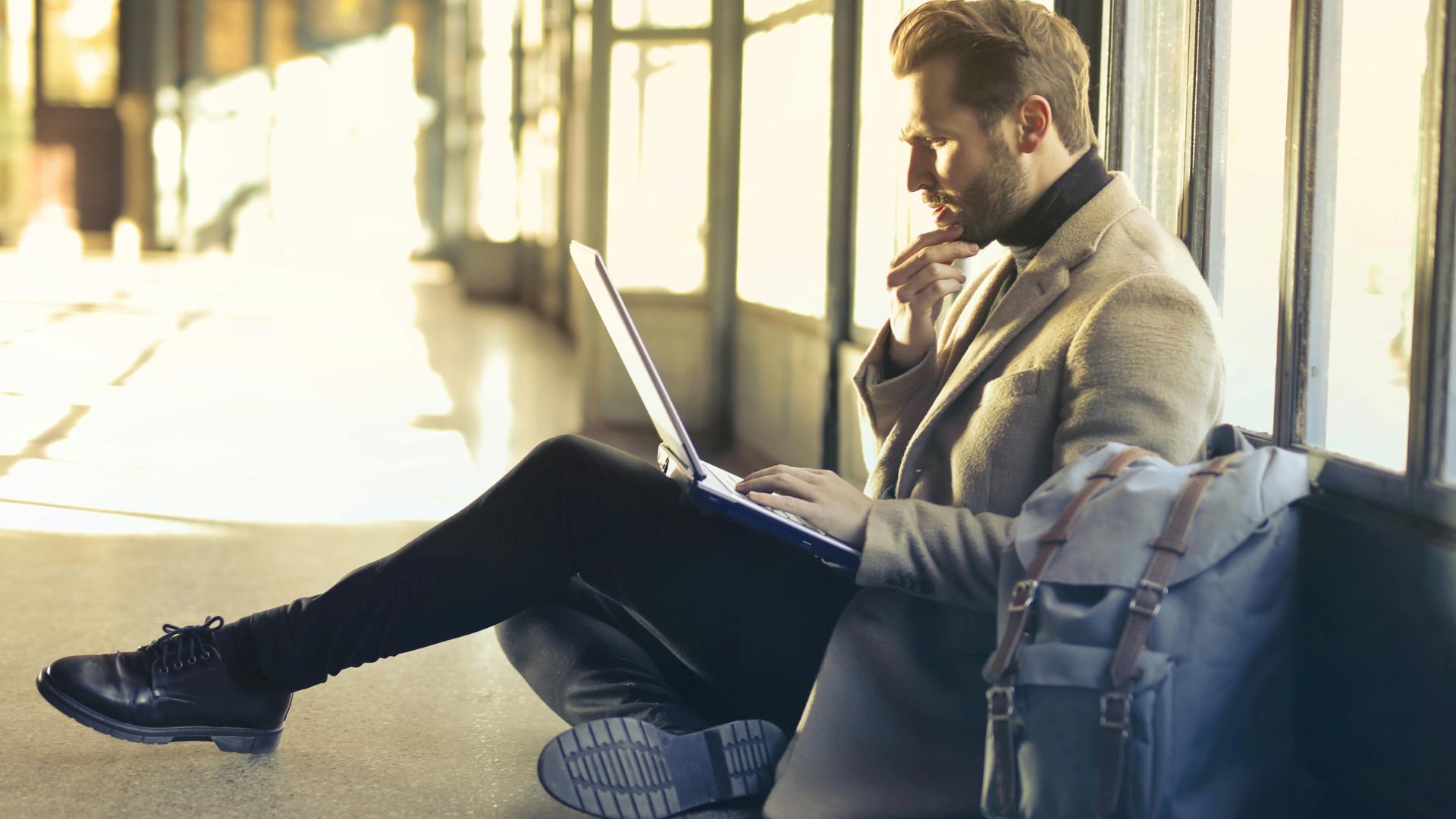 Young man sitting indoors at an airport using laptop. Ideal for remote work themes.