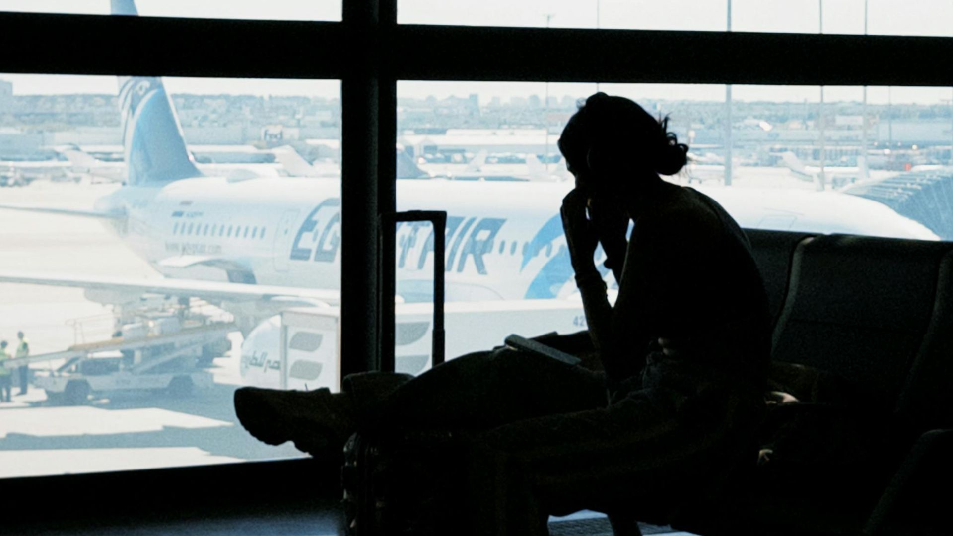 Silhouette of a person at an airport window with airplane view, embodying travel anticipation and solitude.
