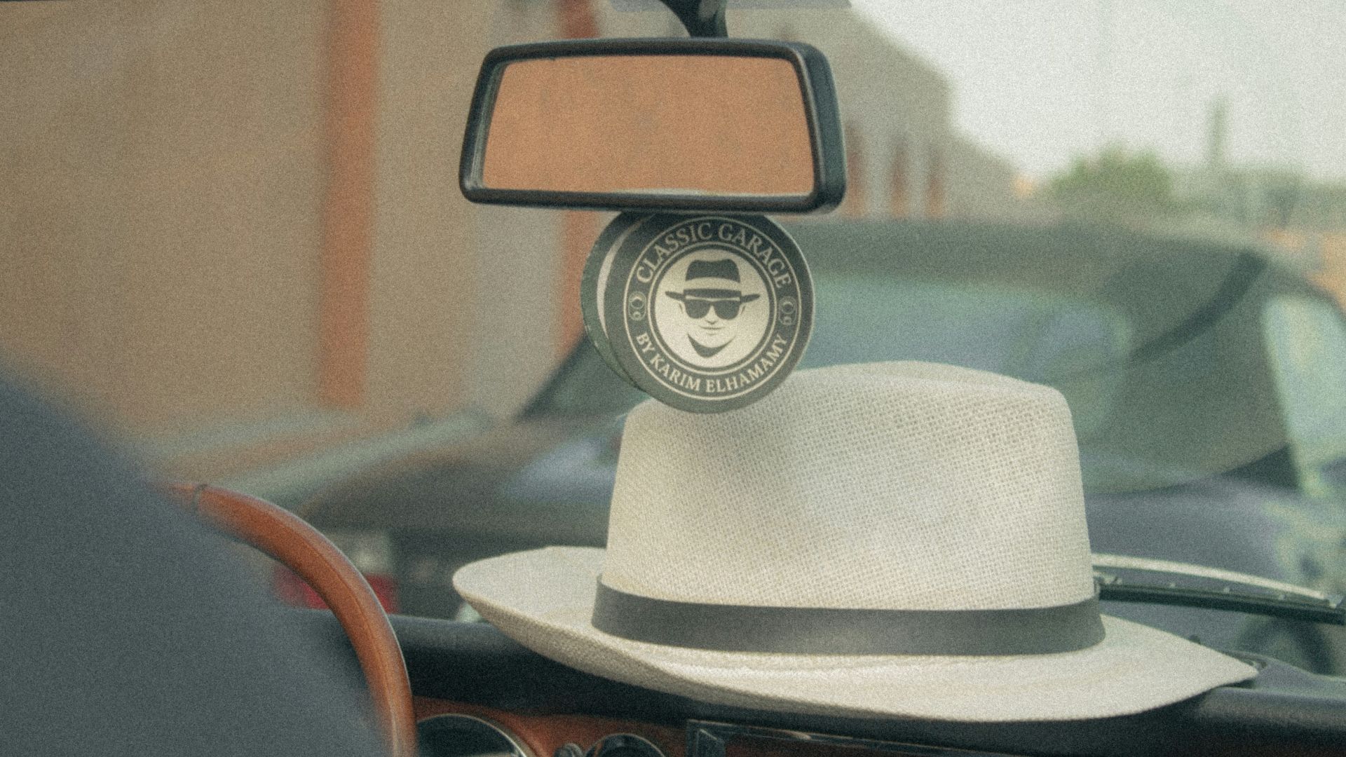 White fedora hat rests on car dashboard with rearview mirror.