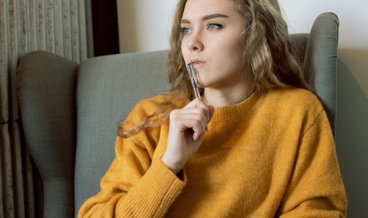 Woman in Yellow Jacket Thinking while Holding a Pen and Notebook