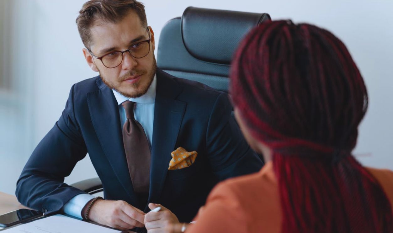 Man in Corporate Attire Sitting In front of a Person with Afro Braids
