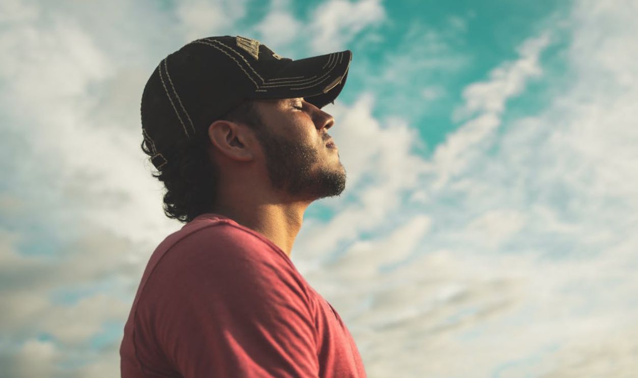 Man Wearing Black Cap With Eyes Closed Under Cloudy Sky