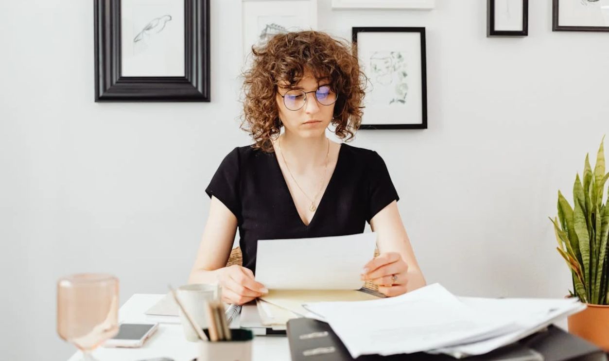 Curly-Haired Woman Wearing Eyeglasses while Holding a Paper