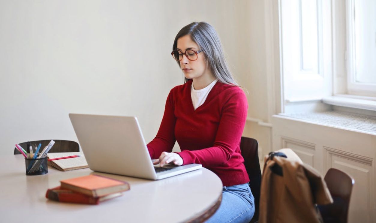 Woman in Red Long Sleeve Shirt Sitting on Chair Using Macbook