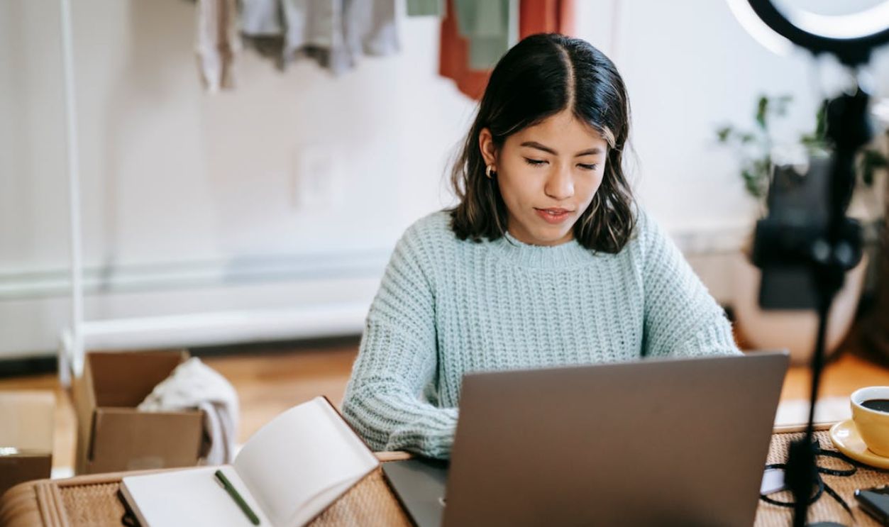 Hispanic lady working remotely on laptop near notebook in room