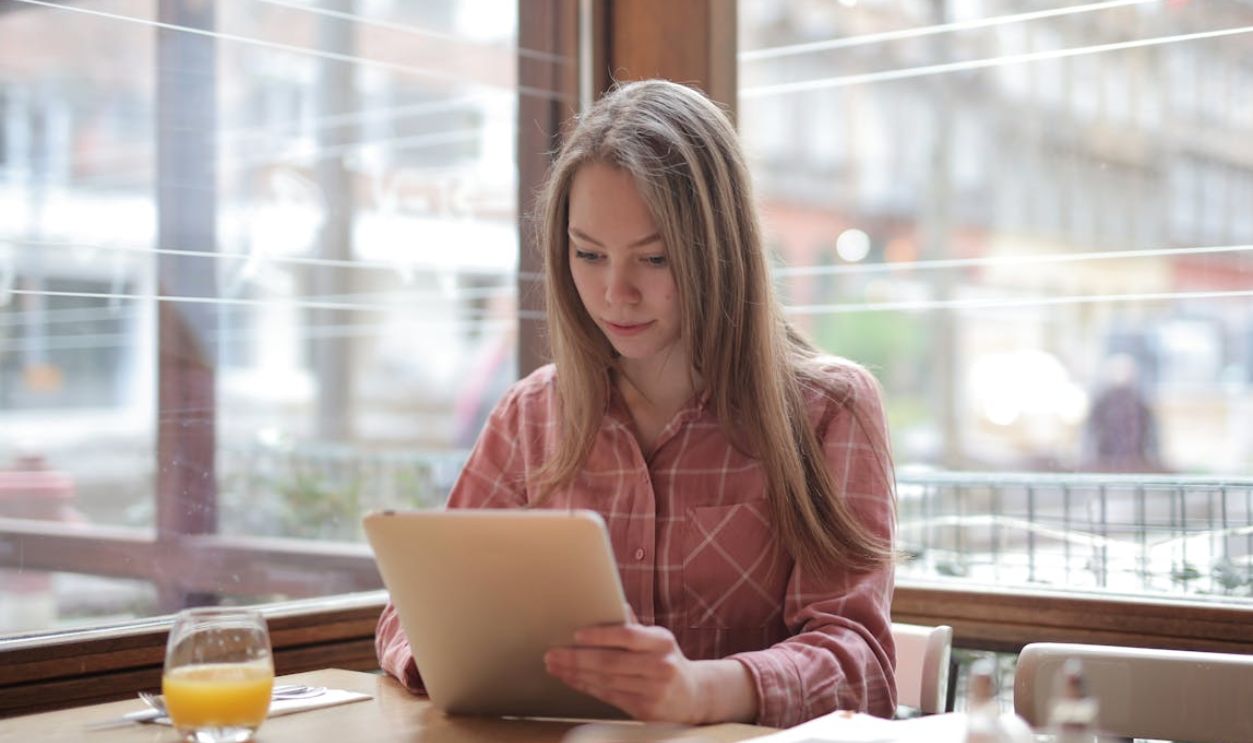Woman in Pink and White Stripe Long Sleeve Shirt Using Silver Ipad