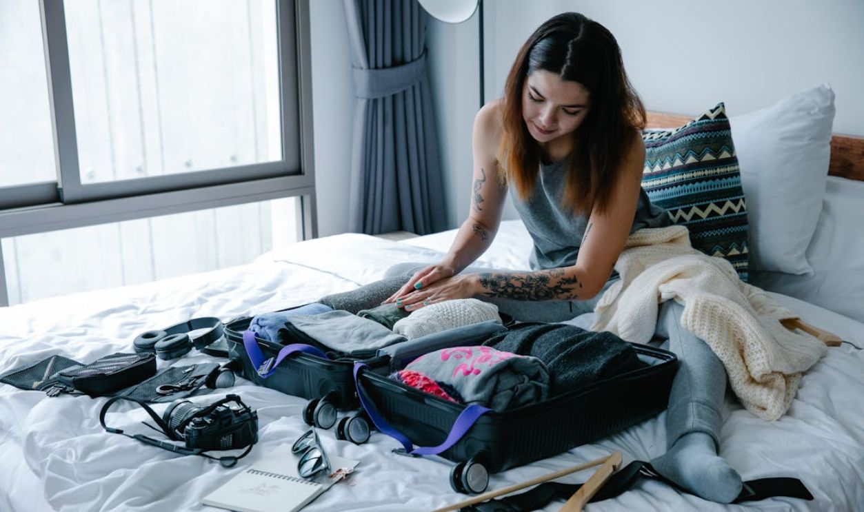 Woman Sitting on Bed at Home Packing Suitcase