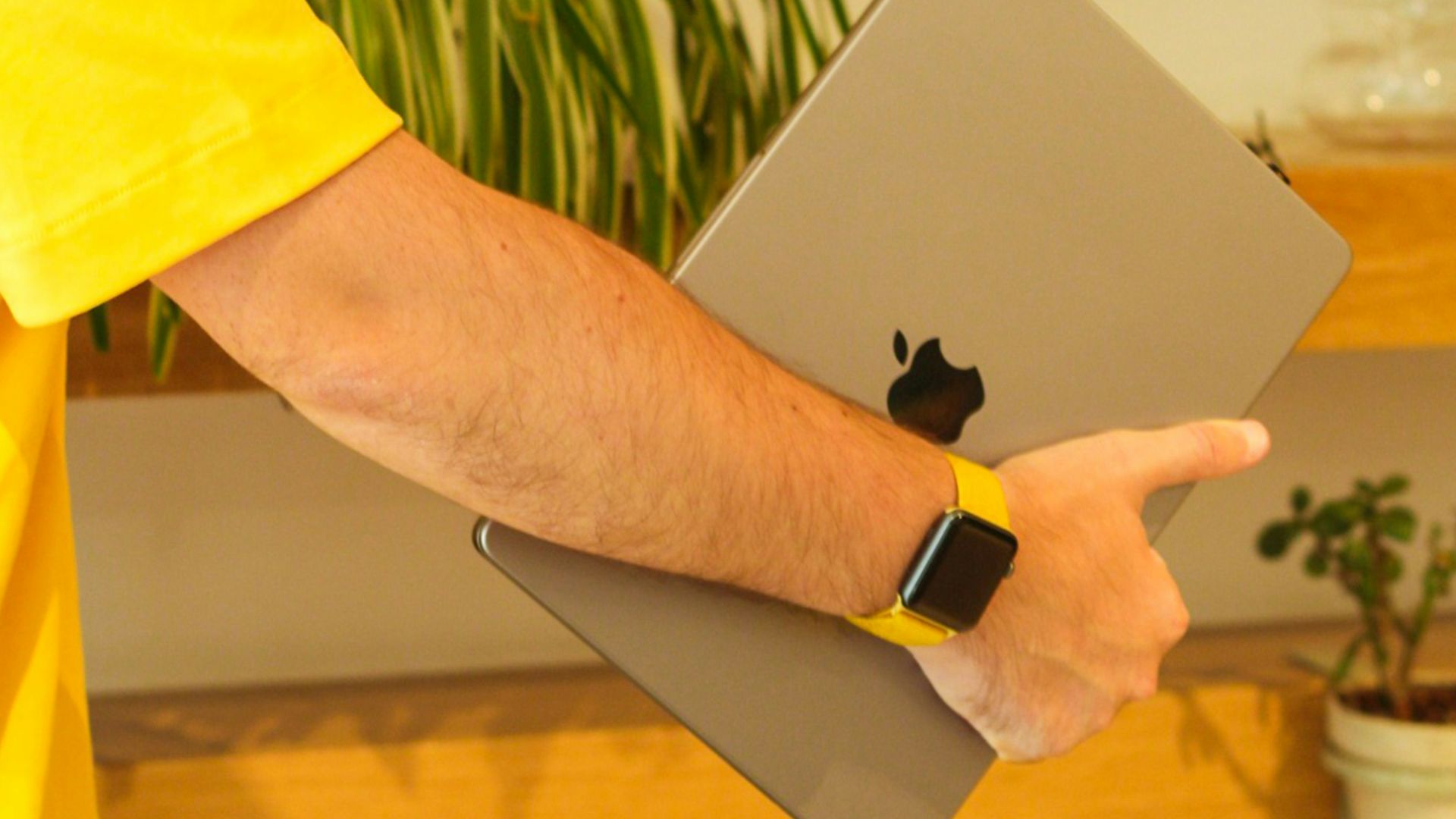 a man in a yellow shirt holding an apple laptop
