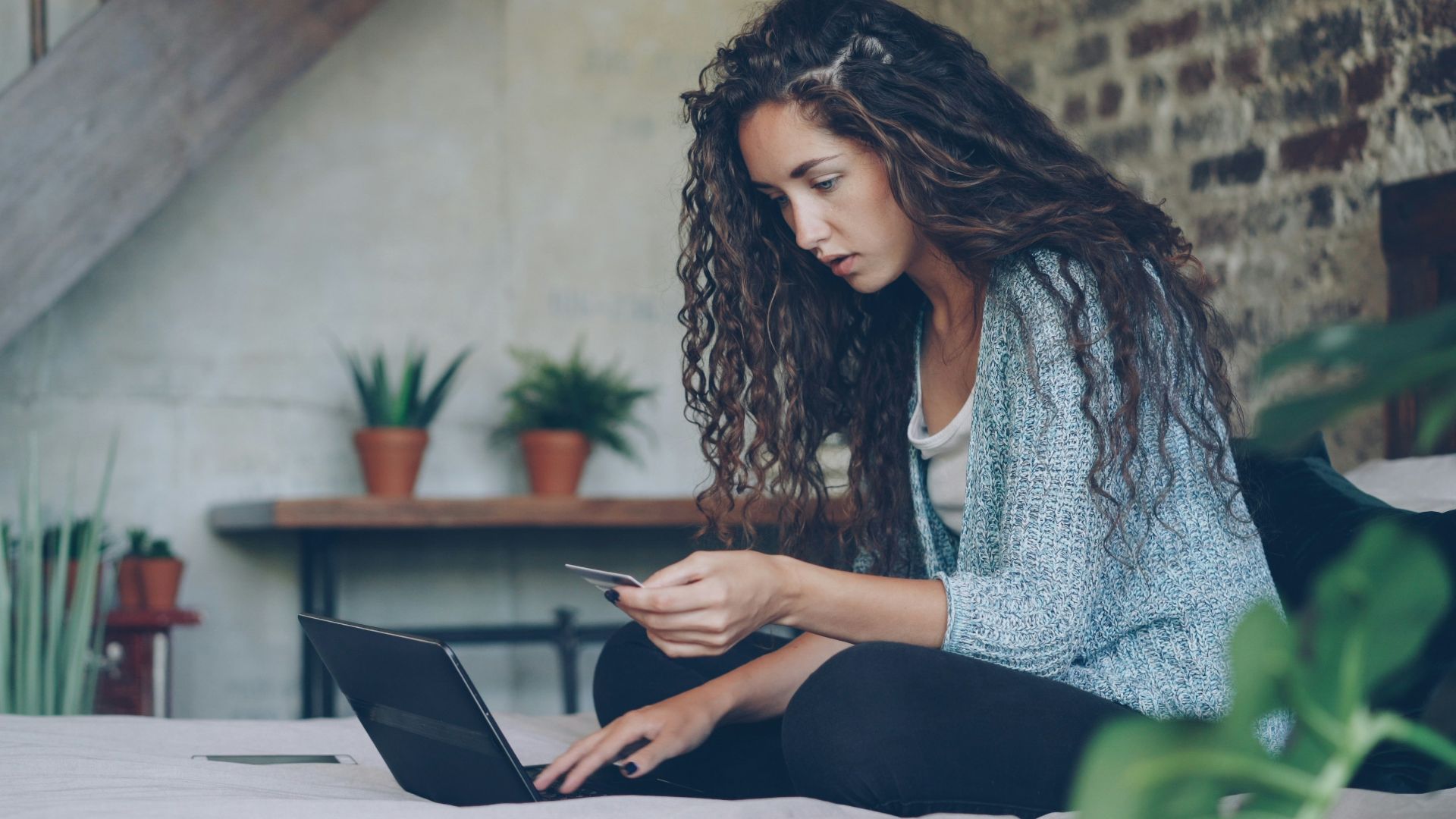 Woman using laptop and credit card on bed.
