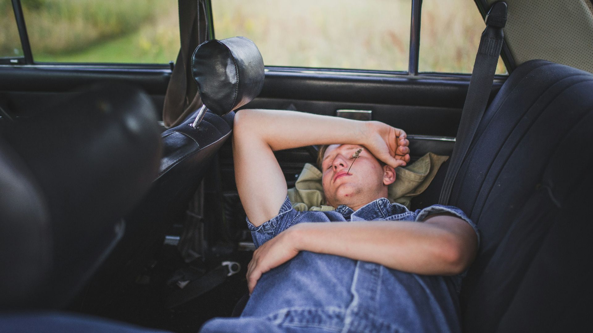 person in blue denim shirt sleeping behind the car seat