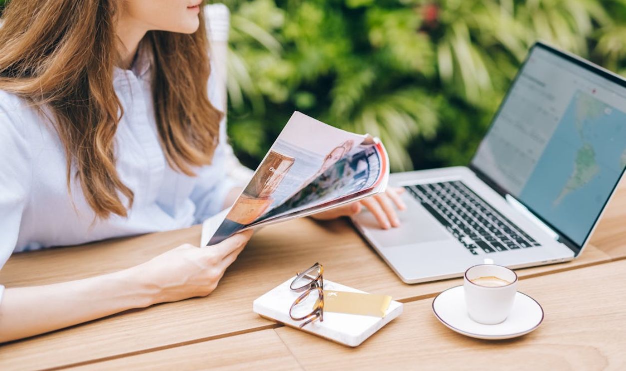 Woman Holding a Magazine While Using a Laptop