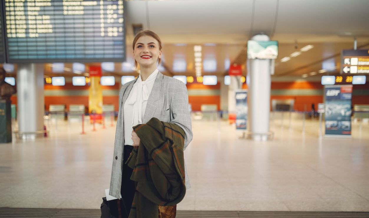 Happy young woman standing with baggage near departure board in airport