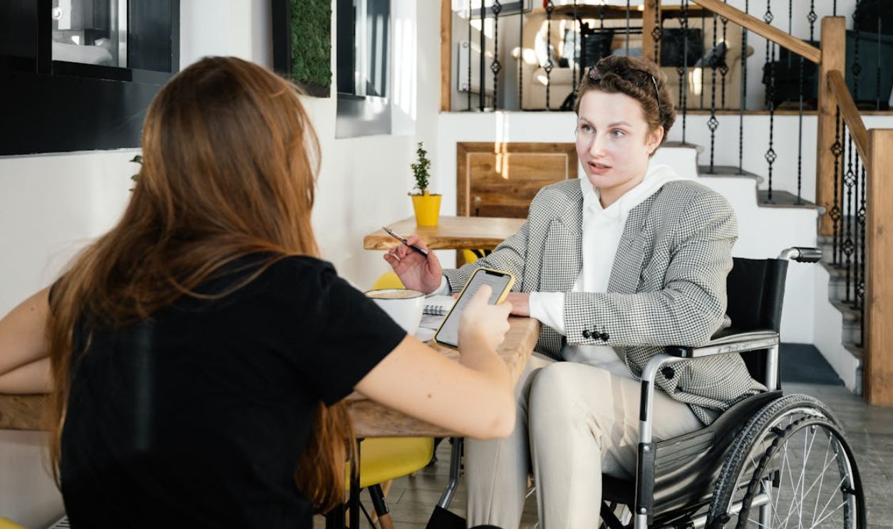 Women in wheelchair communicating with female colleague in cafe