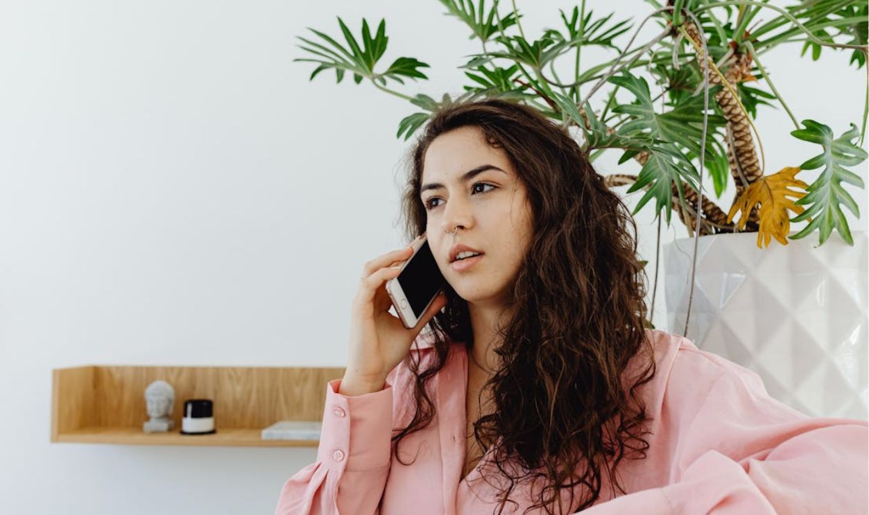 A Curly-Haired Woman in Pink Long Sleeves Having a Phone Call