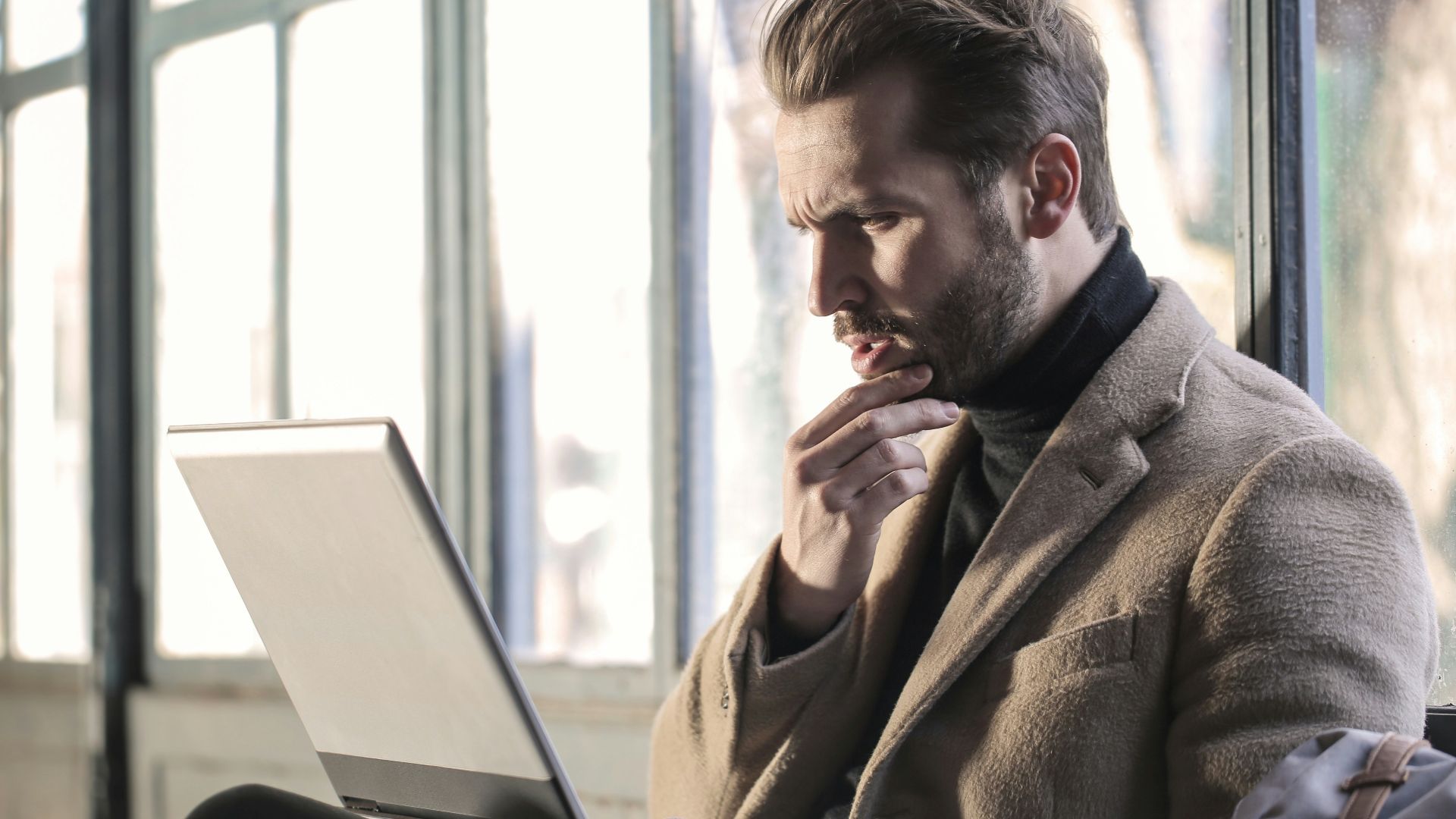 man holding his chin facing laptop computer