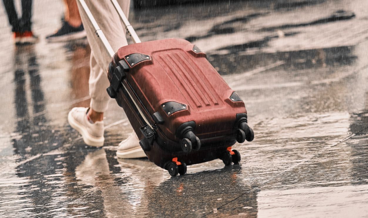 Suitcase close-up carries a girl on a wet road. A lonely man walks on a wet pavement in the rain among people.