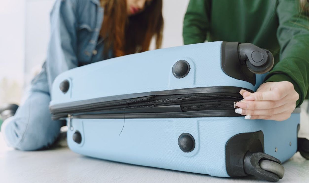 Young women closing luggage bag on floor