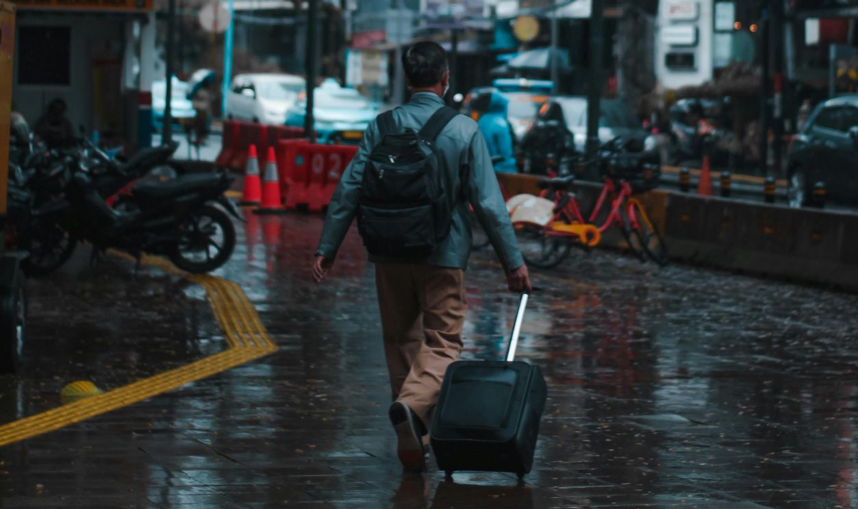 Back View of a Man Walking on Wet Pavement with His Luggage