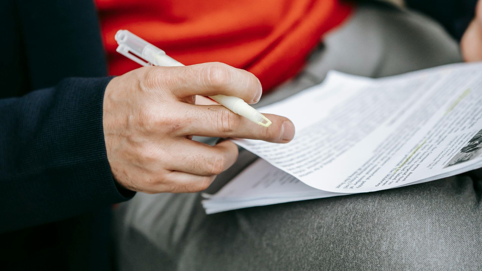 A focused individual reviewing documents outdoors, pen in hand, wearing vibrant clothing.