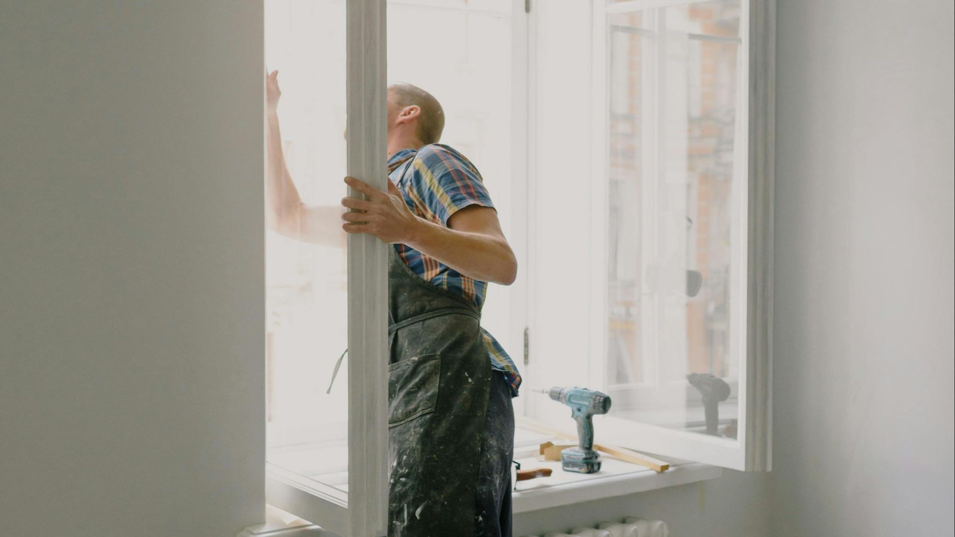 Side view of anonymous handyman in uniform mounting window frame during renovation process in flat