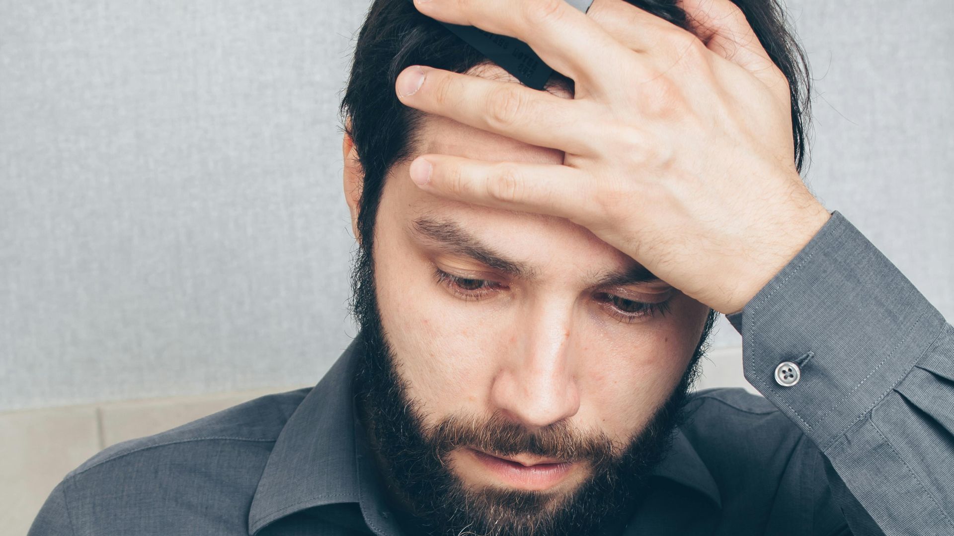A stressed man looks at his smartphone, holding a credit card in his hand.
