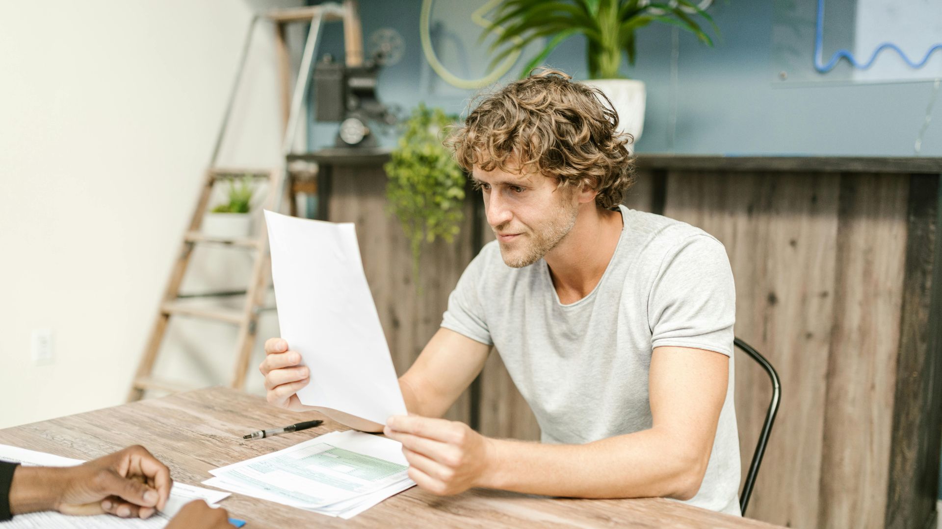 A man with curly hair evaluates documents at a desk, highlighting focused work in a professional setting.