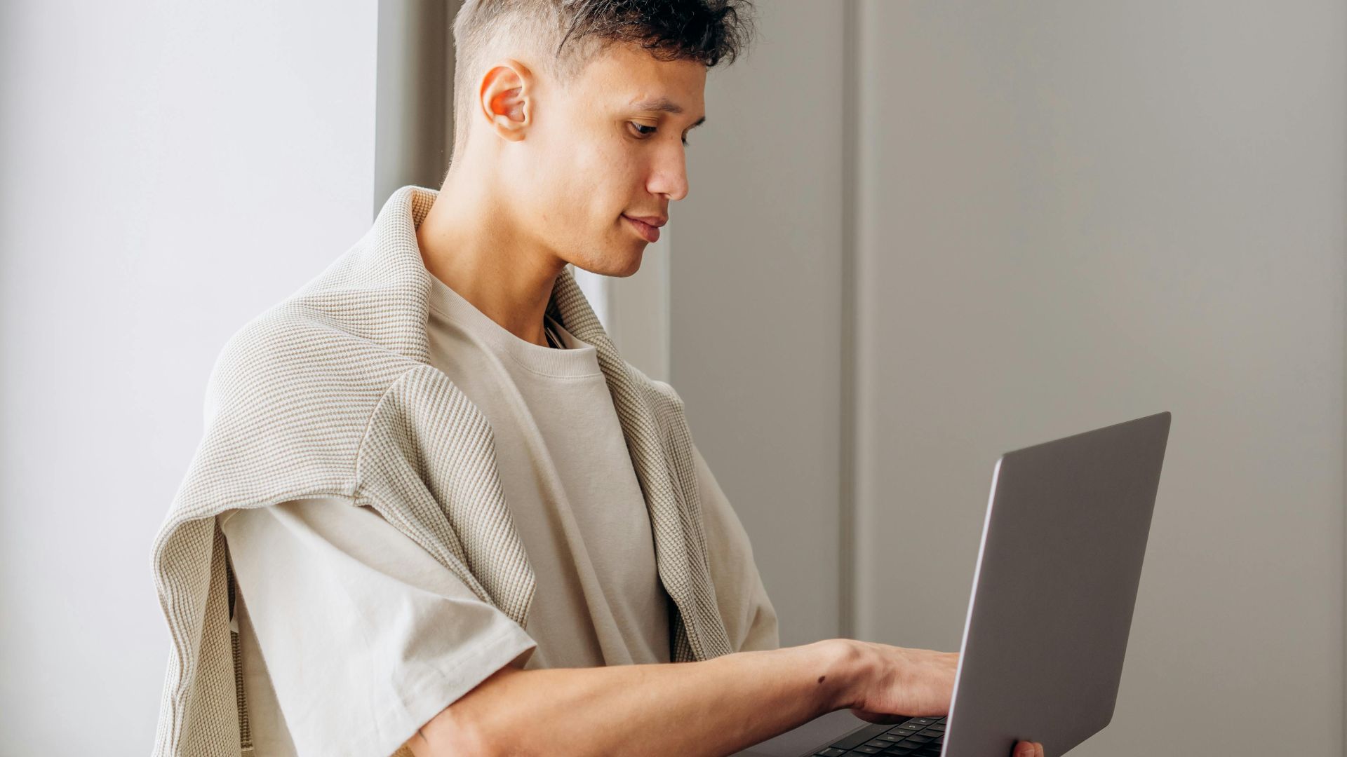 Young man standing by window using a laptop, capturing the essence of modern remote work.