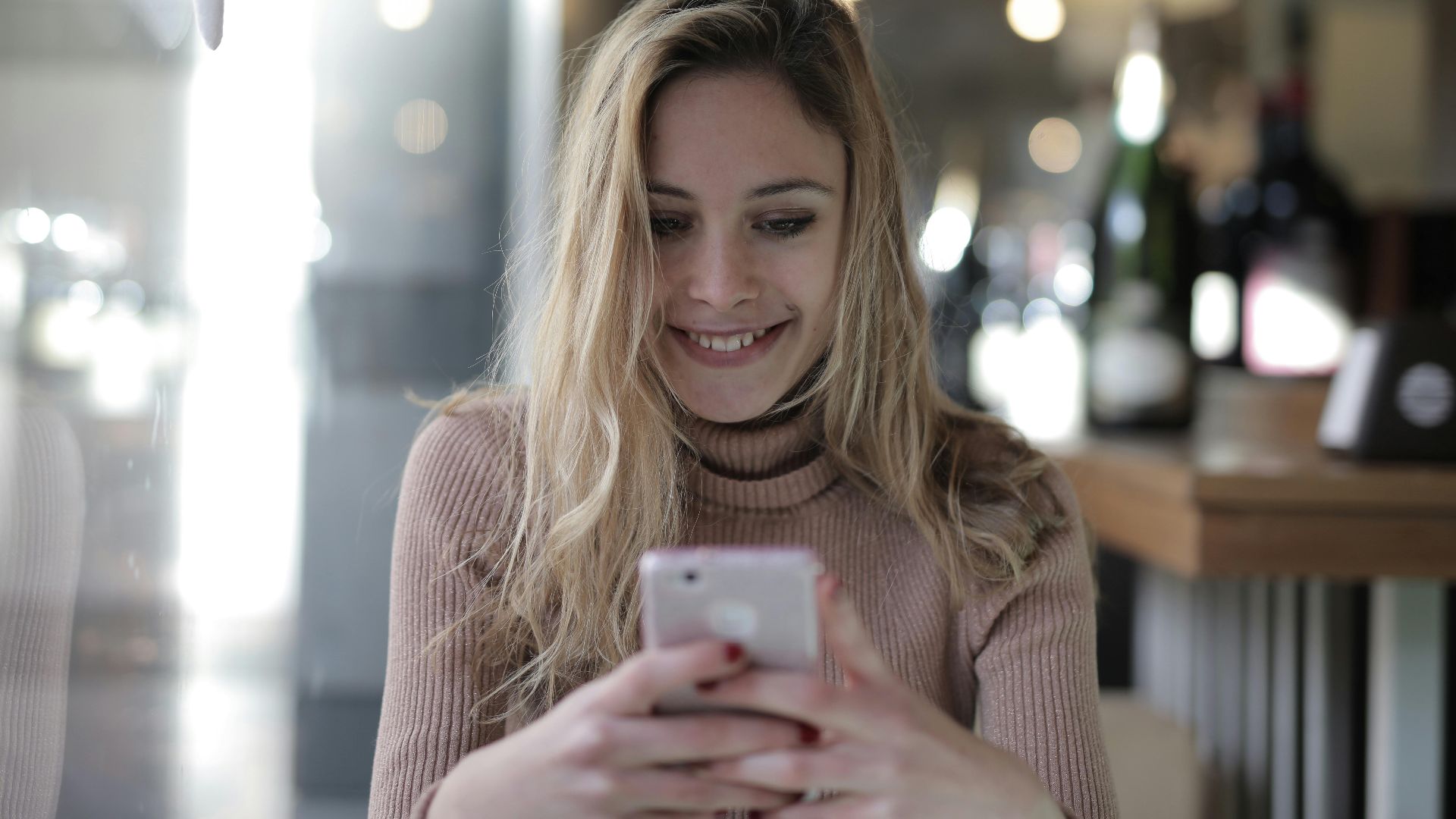 A joyful woman with blonde hair texting on her smartphone in a cozy cafe.