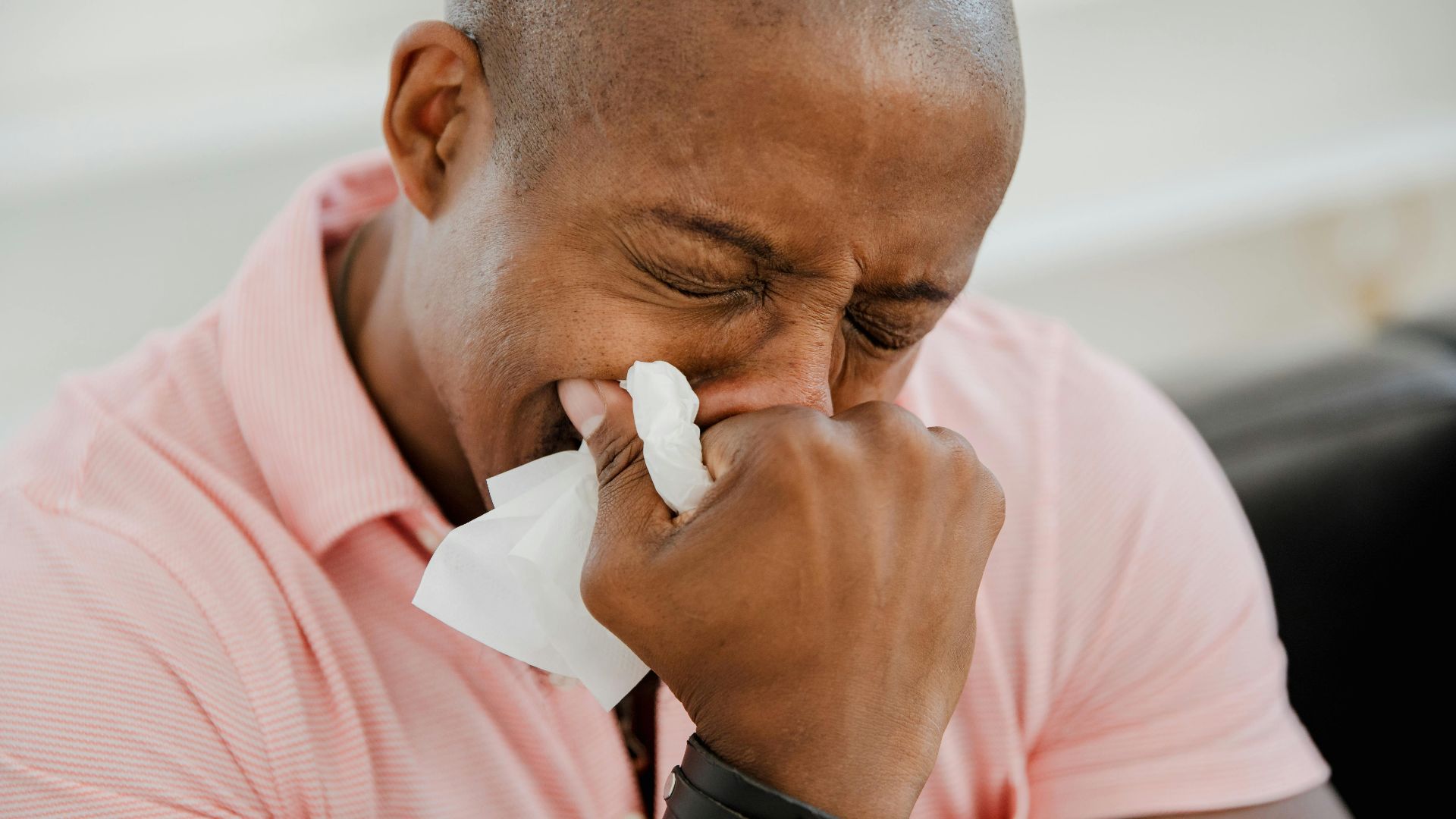A close-up image of a black man in a pink shirt expressing strong emotions.
