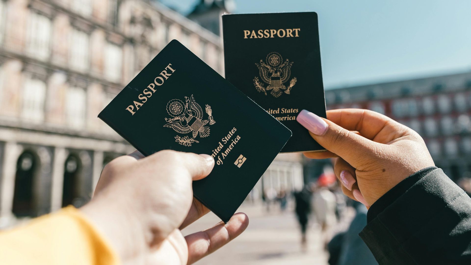 Crop unrecognizable travelers in casual clothes demonstrating passports of United States of America standing on square in historical city district