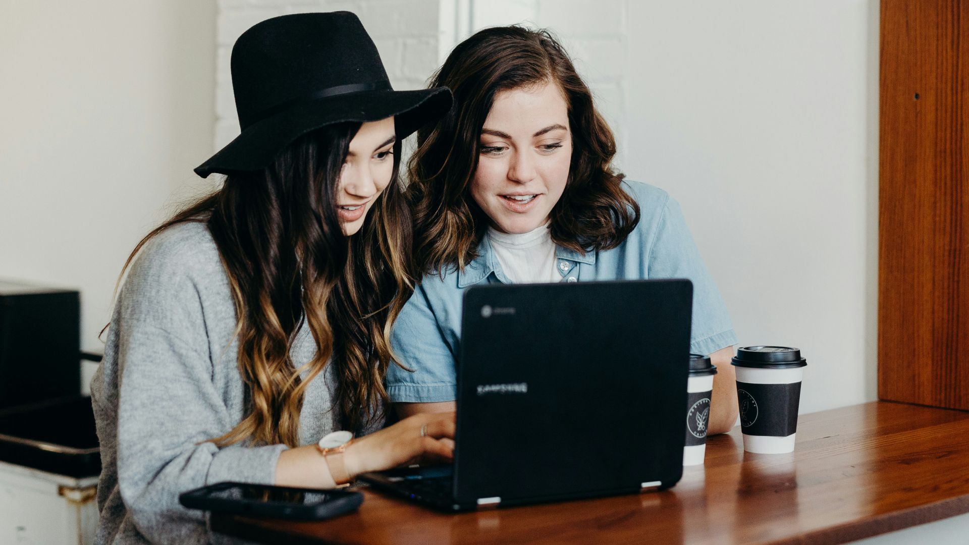 two woman sitting near table using Samsung laptop