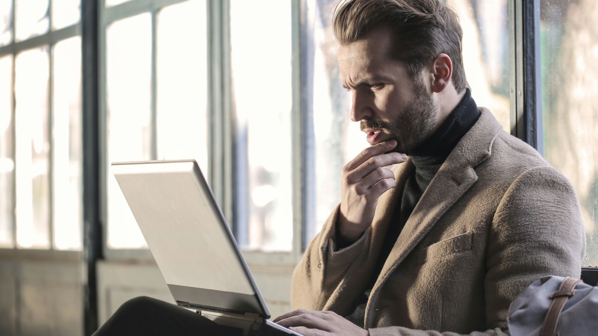 man holding his chin facing laptop computer