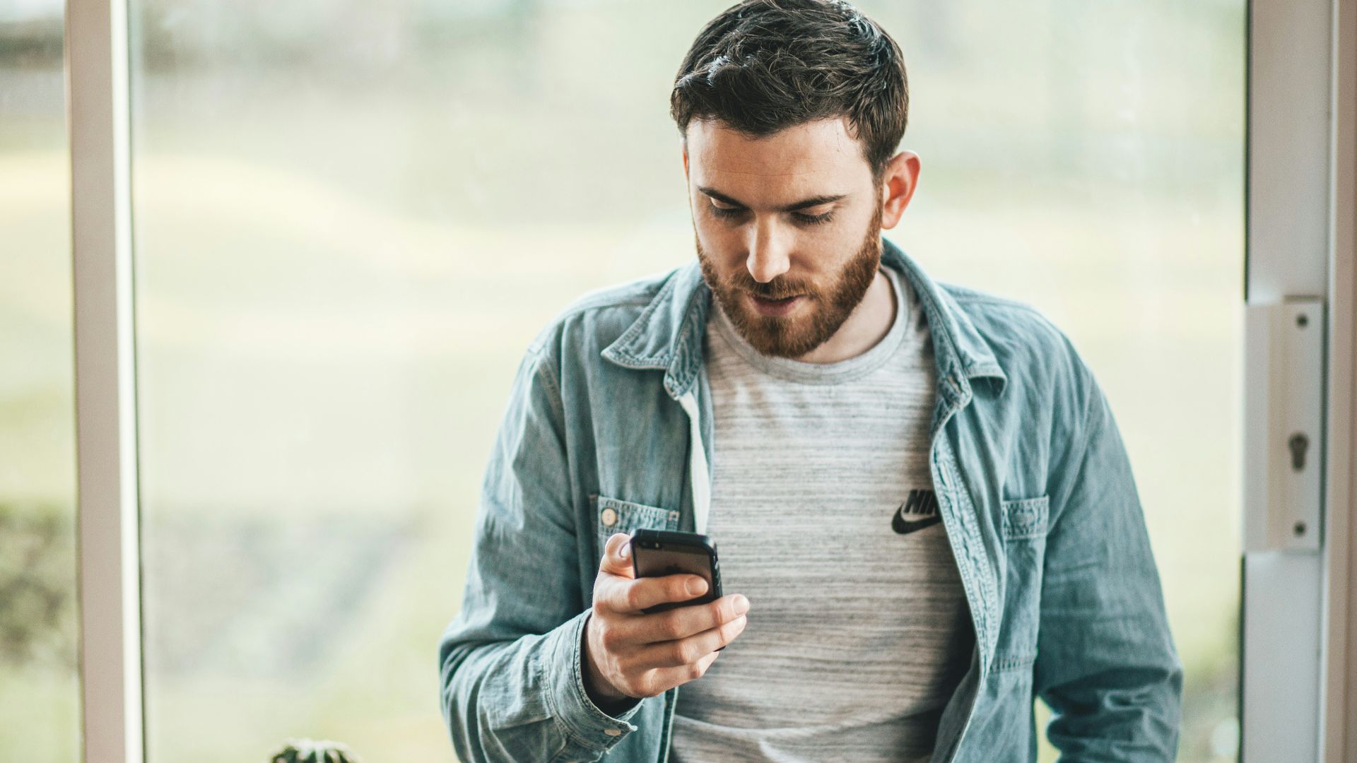 man holding a smartphone near the window