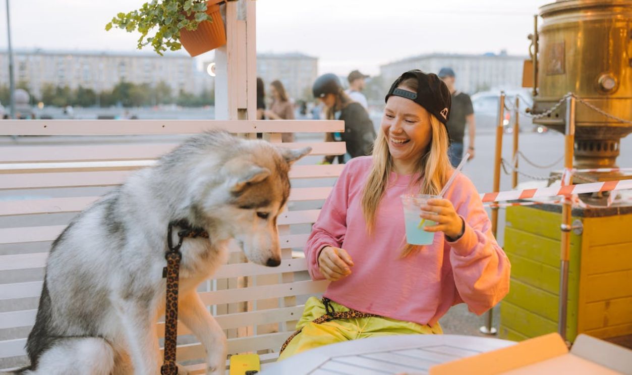 A woman and her husky enjoying a relaxed outdoor moment with a refreshing drink.
