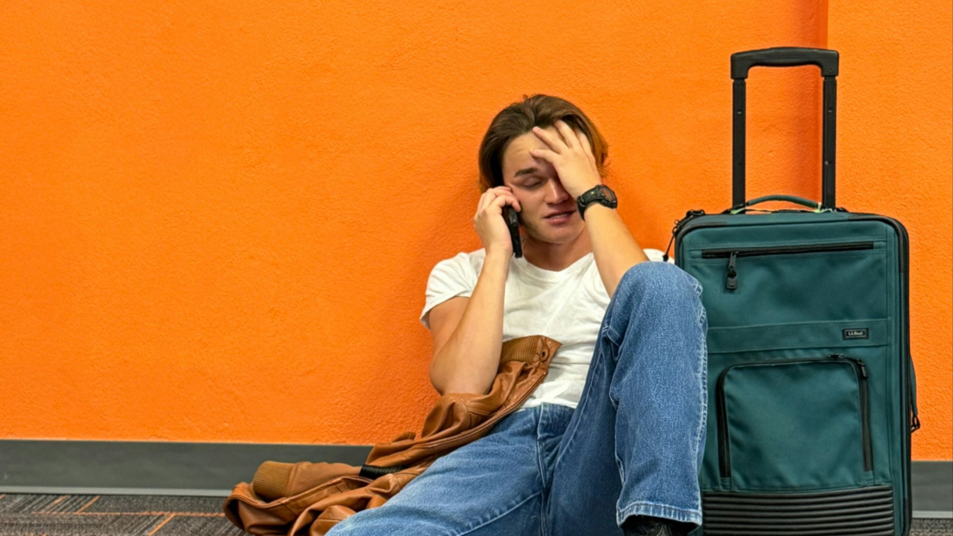 Man sitting on floor with suitcase, looking distressed.