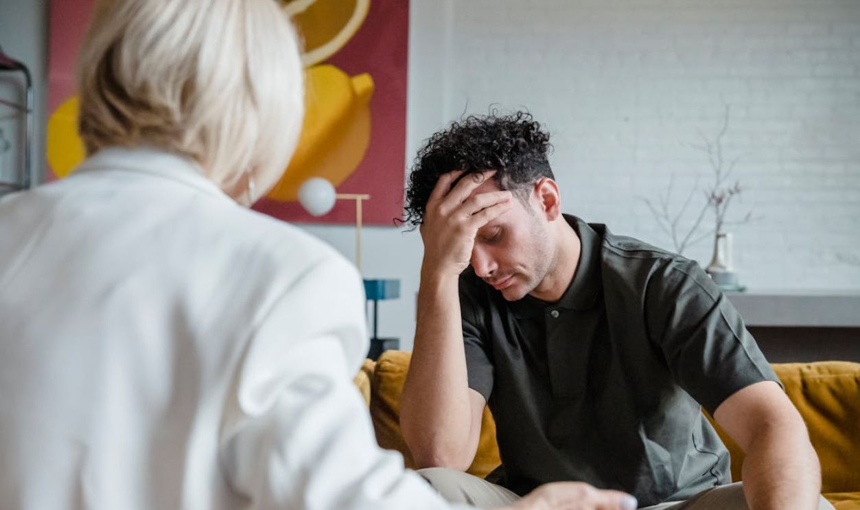 A young man in a therapy session, expressing emotions with hand on forehead
