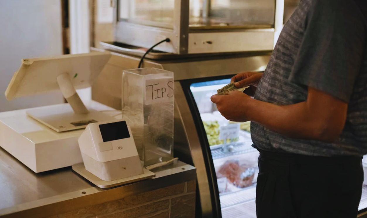 Close-up of a person making a cash payment at a store counter with a digital register.