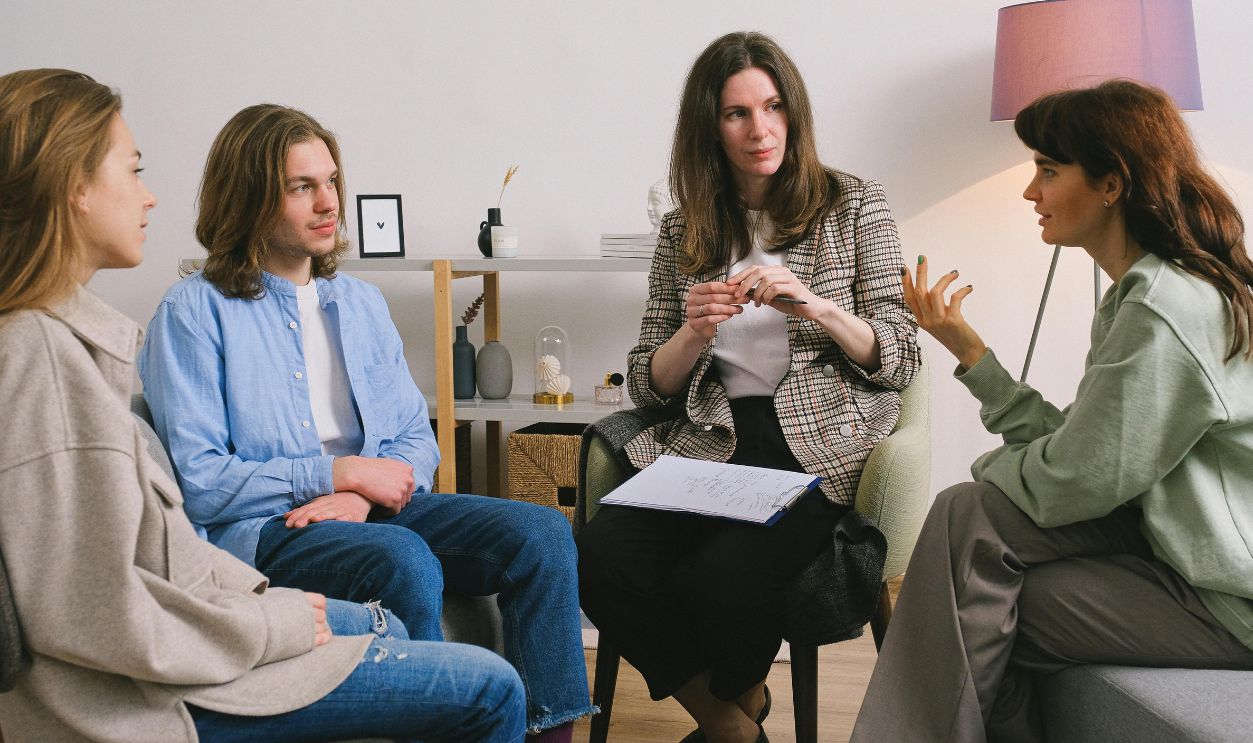 A group therapy session taking place indoors with an attentive counselor guiding the discussion